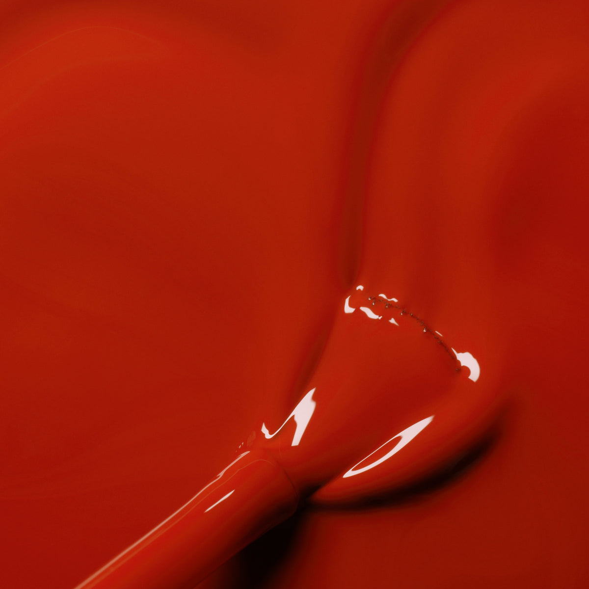 Gros plan d’un pinceau plongé dans Indian Summer de Manucurist, un vernis gel rouge brique brillant, avec une couleur rouge brique lisse et brillante étalée sur la surface.