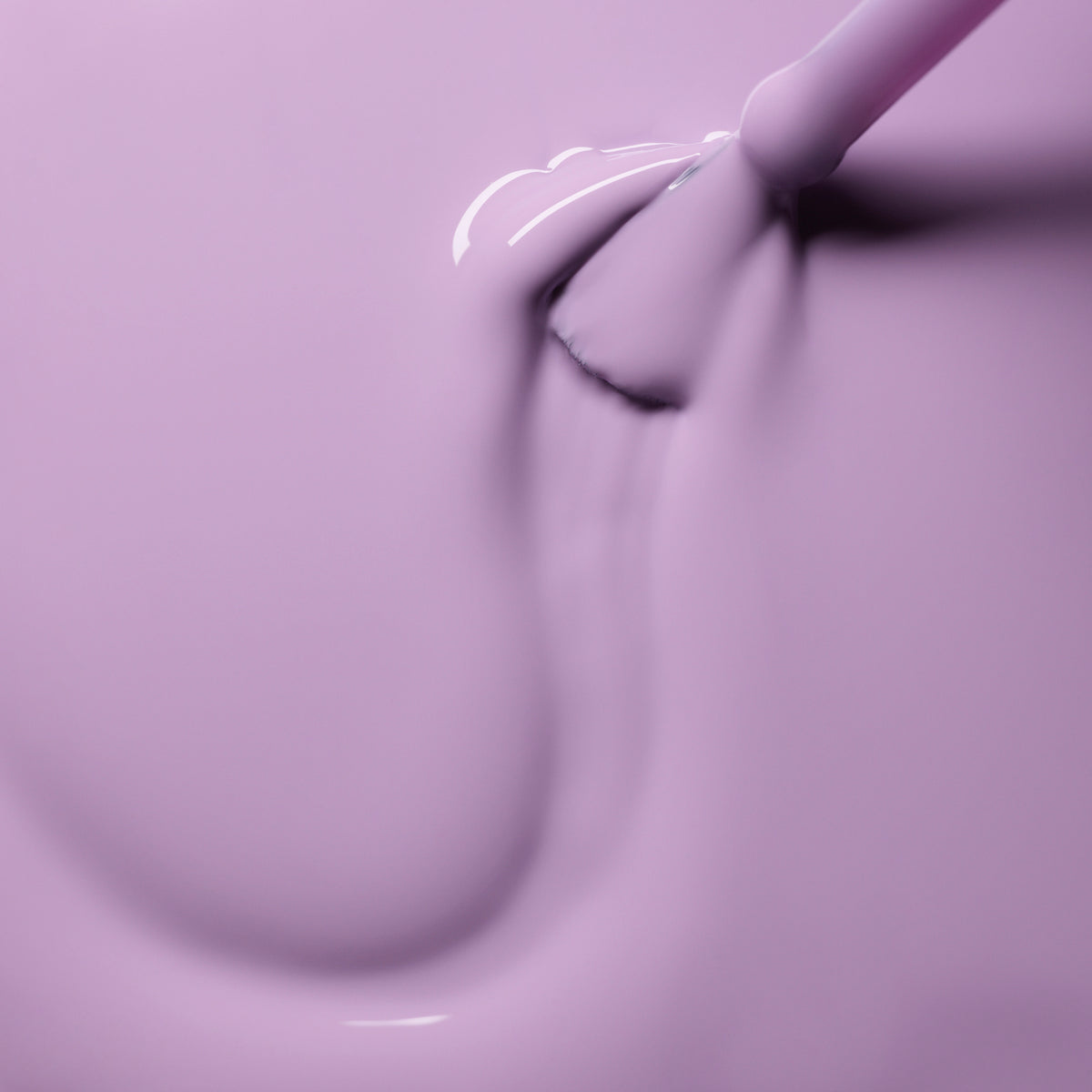 A close-up of a brush applying smooth, glossy Lisa Lilas nail polish from Manucurist in sweeping strokes on a flat surface.