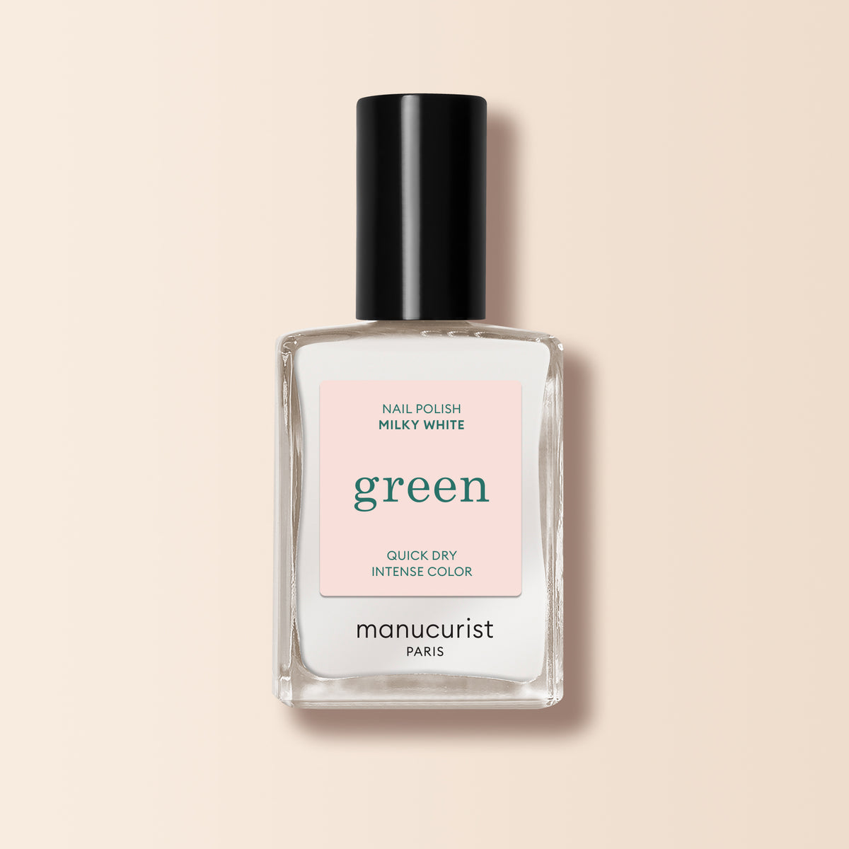 A clear glass bottle of Milky White nail polish by Manucurist with a black cap stands upright on a pale beige background.