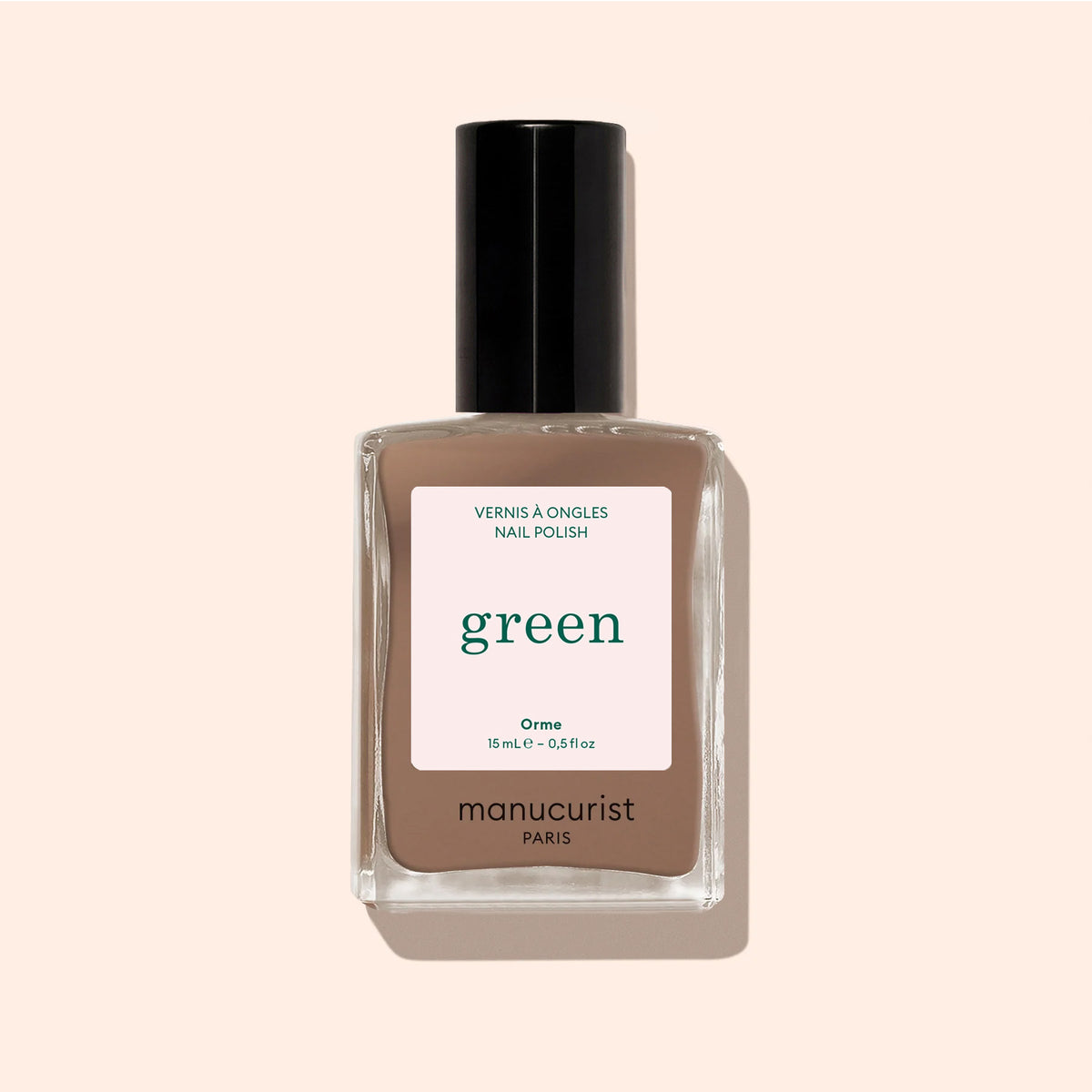A bottle of Manucurist Orme nail polish from the Green™ range, in a café au lait light brown shade with quick-dry, intense color, black cap, and minimalist label displayed on a beige background.