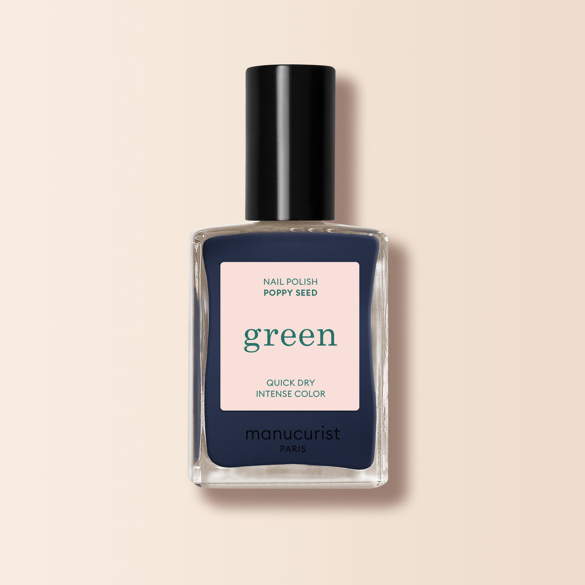 A bottle of Manucurist nail polish in the "Poppy Seed" shade—a dark greyish blue—with a black cap and a label reading “green, quick dry, intense color” is shown against a light beige background.