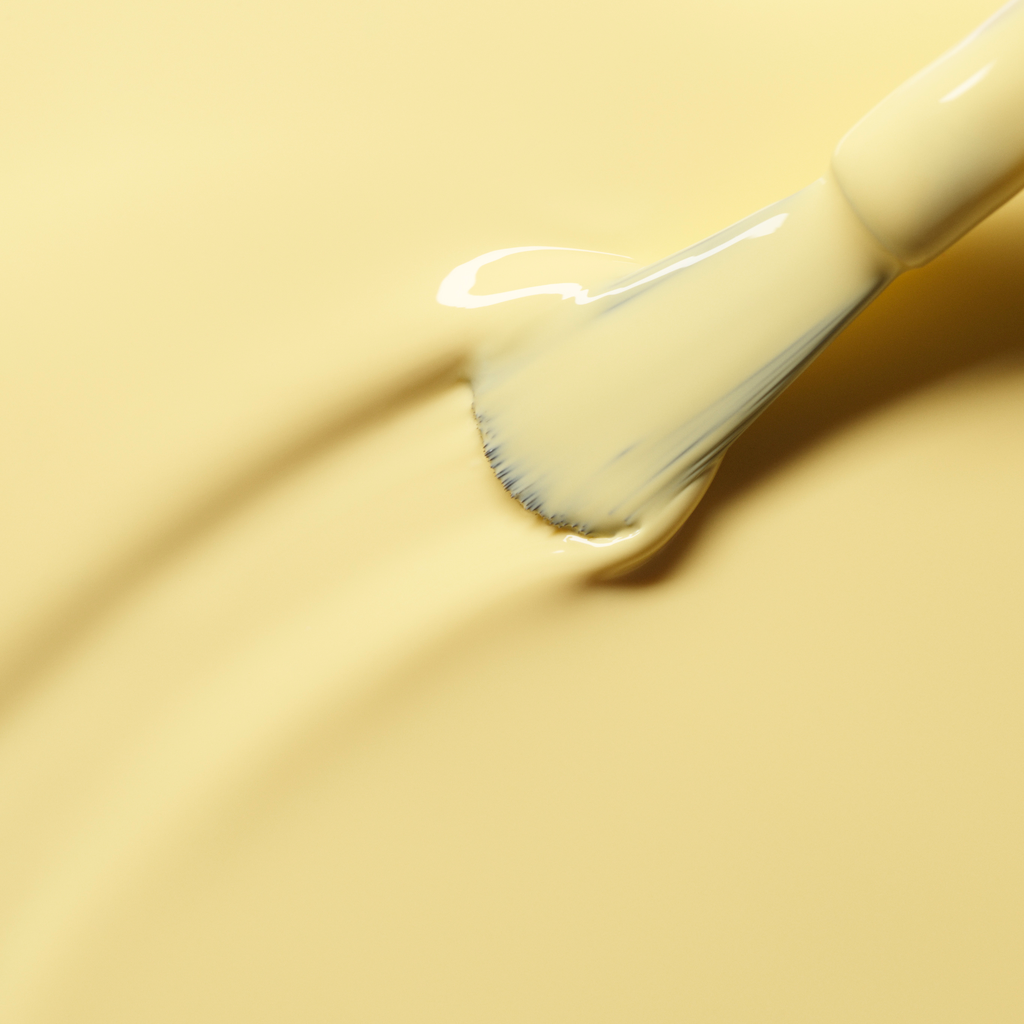 Gros plan d’un pinceau appliquant le vernis à ongles Mimosa jaune pastel et lisse de Manucurist en couches régulières sur une surface jaune assortie.