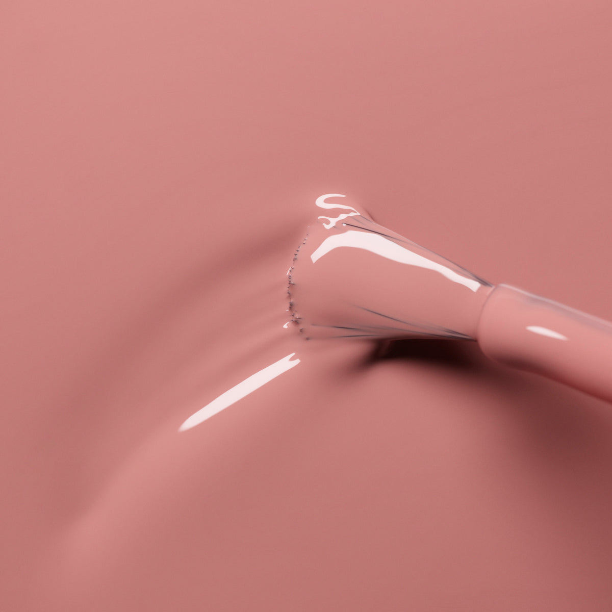 A close-up of a nail polish brush applying Manucurist Old Rose, a smooth, glossy antique powder pink shade, onto a matching pink surface.