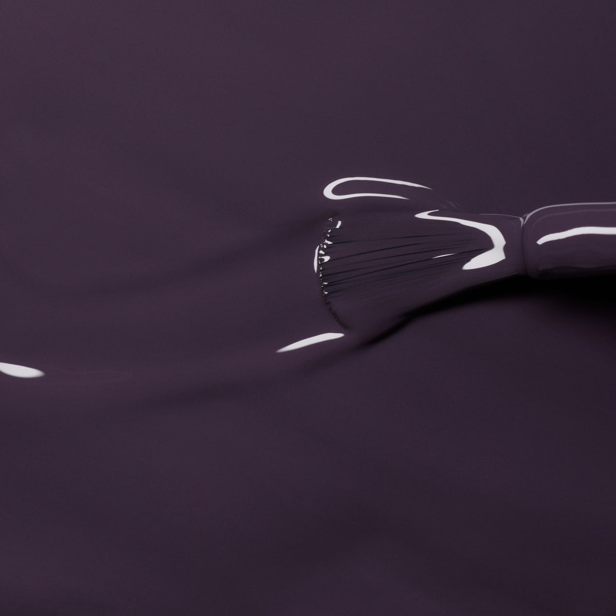 A close-up of a brush applying Manucurist’s Queen of Night, a glossy deep purple nail polish, creating smooth, shiny strokes on the nails.