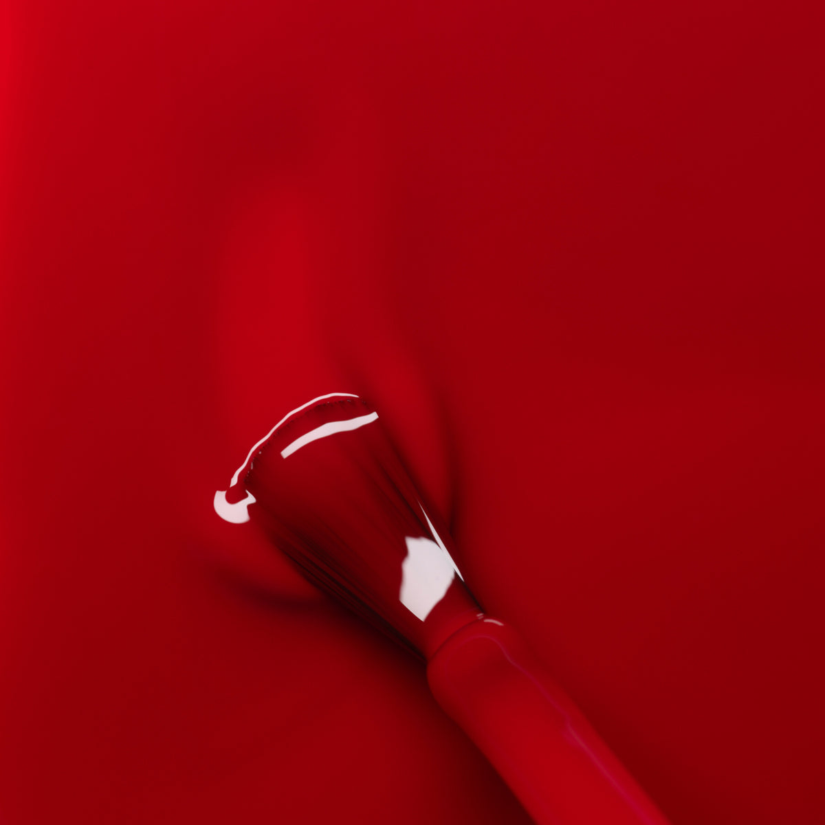 Gros plan sur le pinceau de vernis à ongles Red Cherry de Manucurist étalant une couleur rouge vibrante sur une surface brillante, créant des traits lisses et uniformes avec une finition brillante.