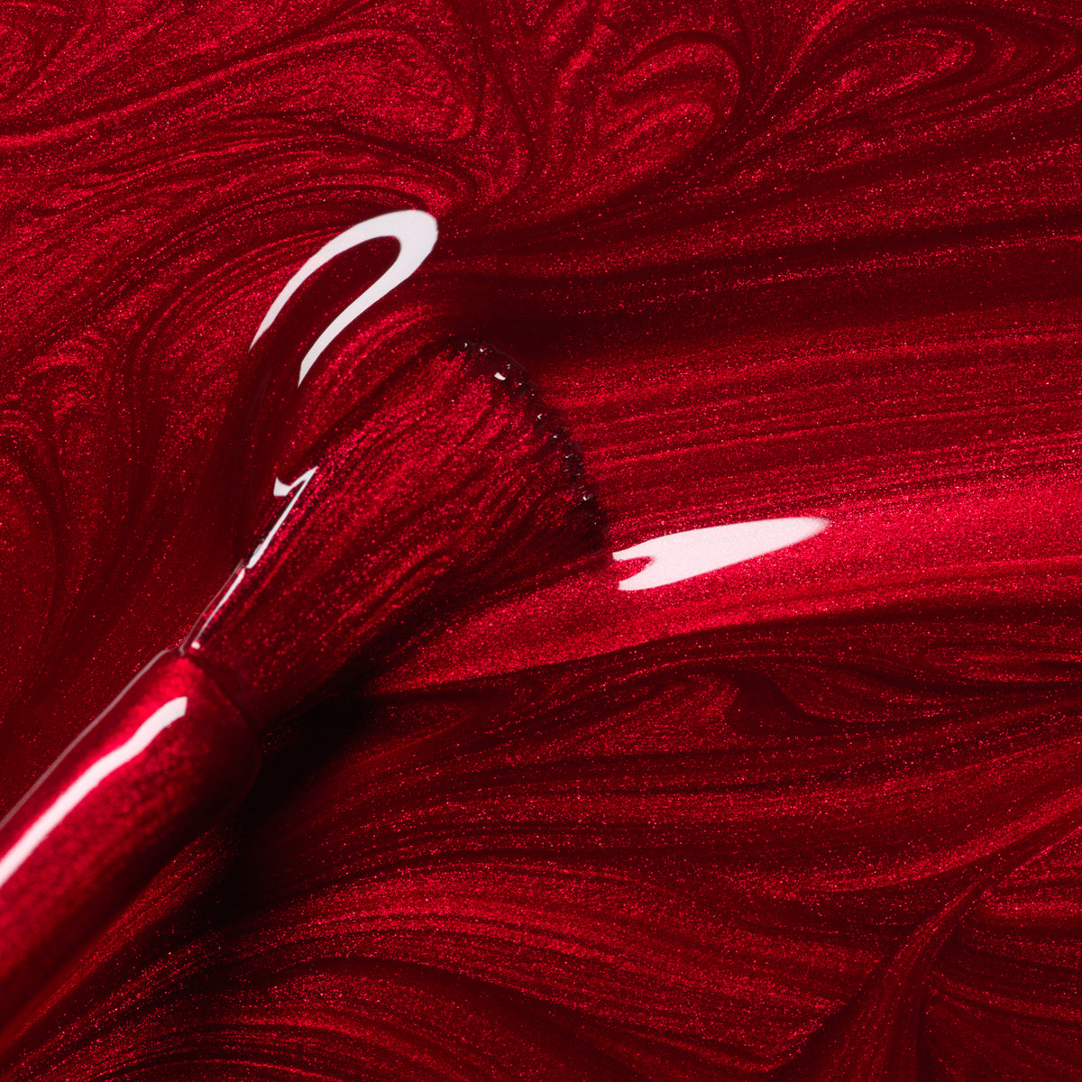 A close-up of the Manucurist Red Hibiscus nail polish brush, coated in chic red polish, with vibrant swirls reflecting light beneath it.