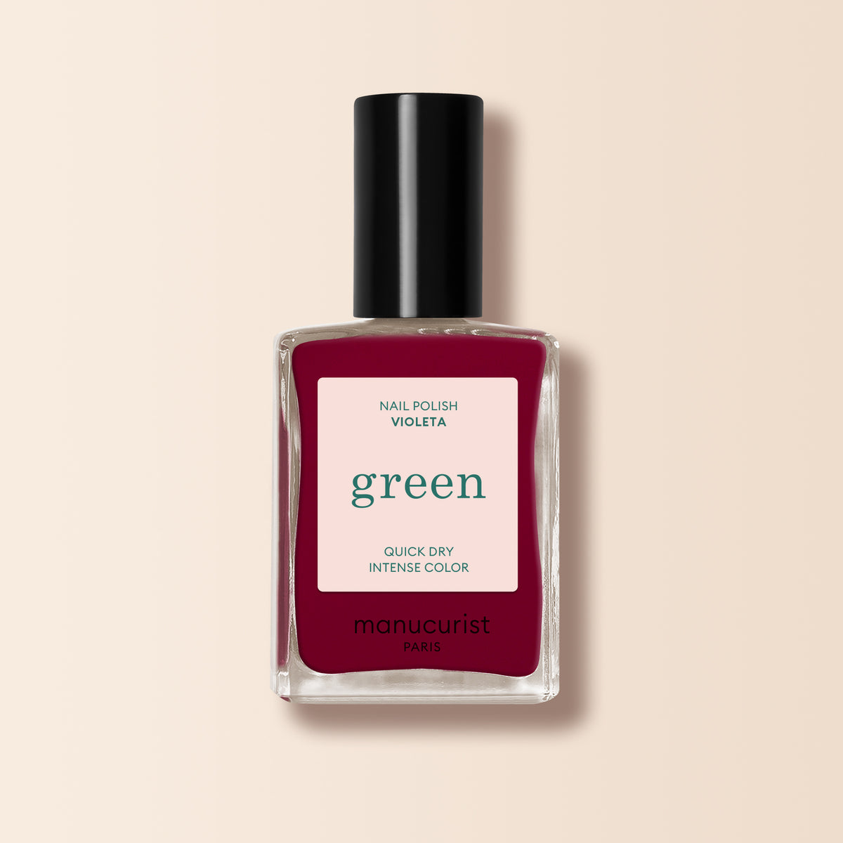 A clear bottle of Manucurist Violeta nail polish with a black cap, from the Green™ range, Quick Dry Intense Color. The deep burgundy purple shade stands out against a soft beige background.