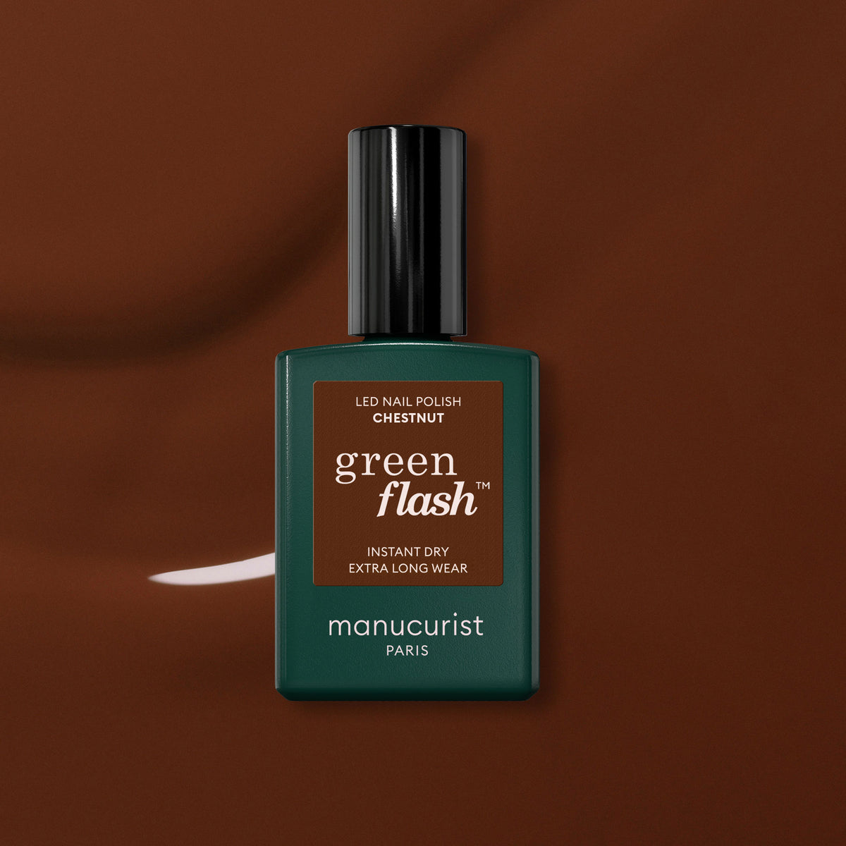 Un flacon vert Manucurist de vernis gel Green Flash™ en Chestnut, une teinte brun chaud, est posé sur un fond brun brillant.