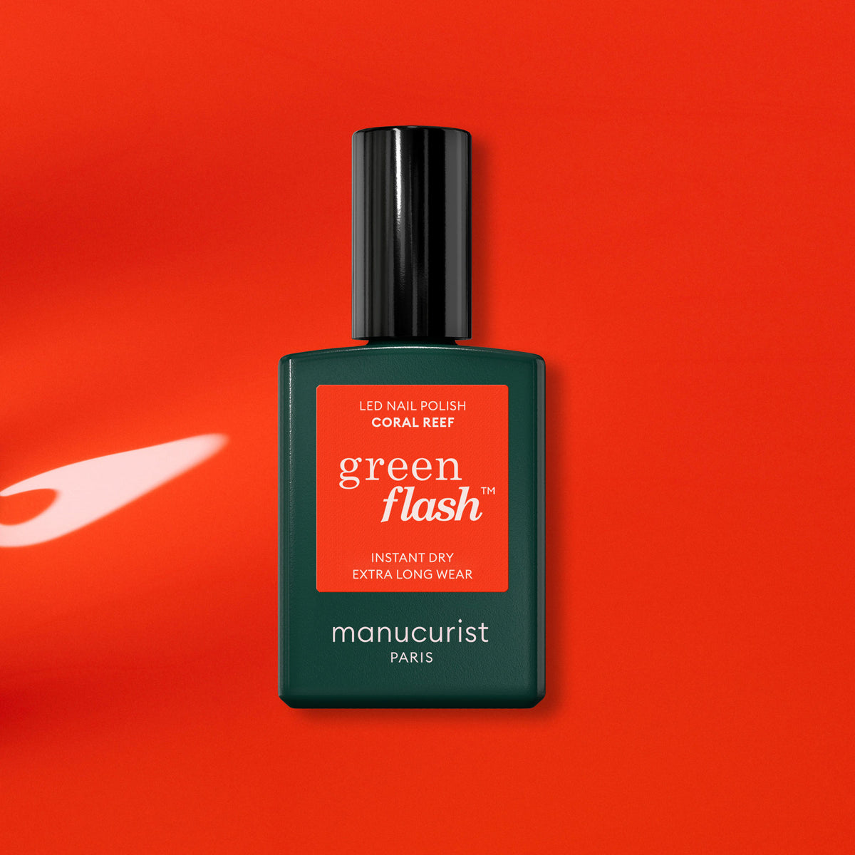A Manucurist Coral Reef Green Flash LED gel polish bottle, featuring a dark green base and red label, rests on a vibrant orange-red surface with soft reflections.