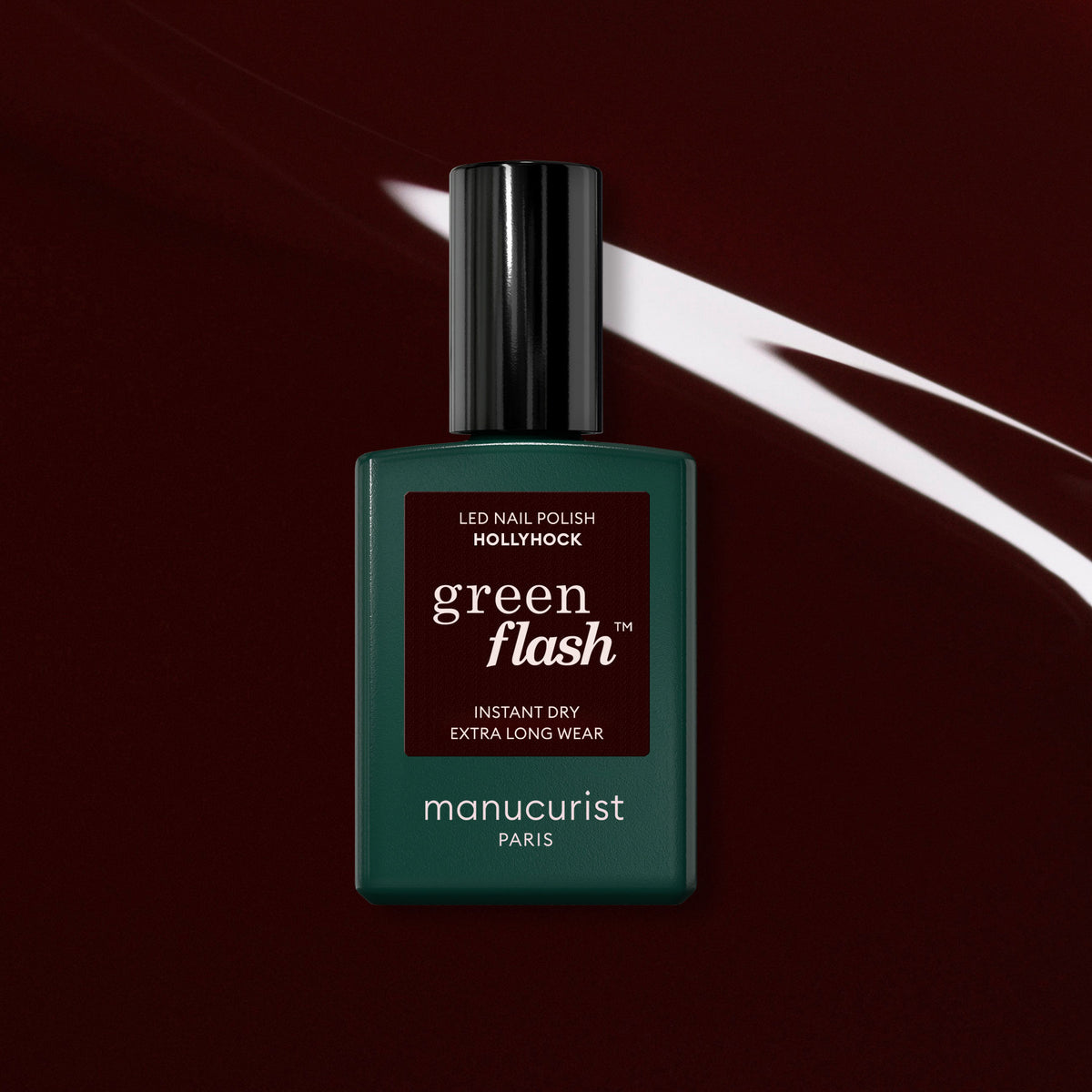 Le vernis semi-permanent Hollyhock de Manucurist se détache sur un fond bordeaux foncé traversé d’un rayon de lumière blanche, révélant la superbe teinte noir-rouge de cette couleur de la collection Green Flash.