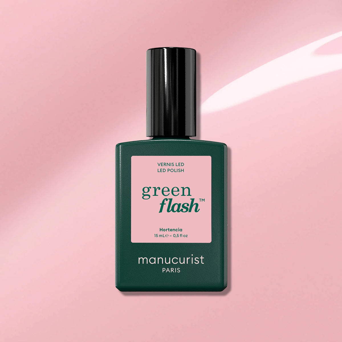 A bottle of Manucurist gel polish in the shade Hortencia rests on a pink background, showing its label “Instant dry, extra long wear.”.