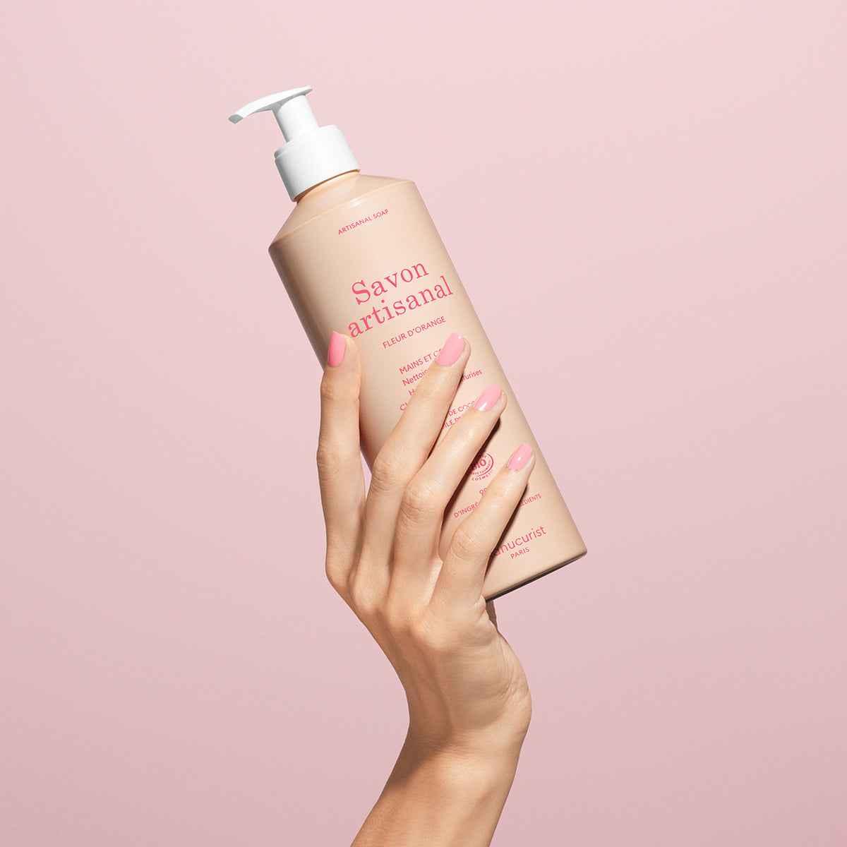 Une main aux ongles manucurés roses tient un flacon à pompe de gel lavant mains et corps bio Manucurist Fleur d&