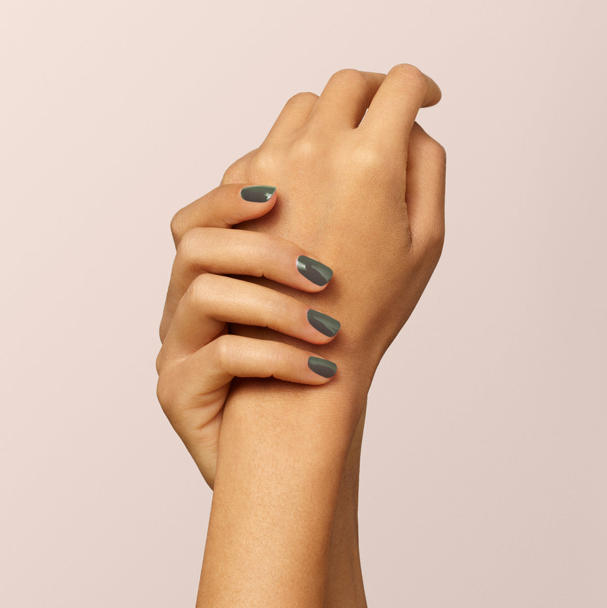Two medium-toned hands rest on a light beige background. Their short nails are painted with Manucurist&