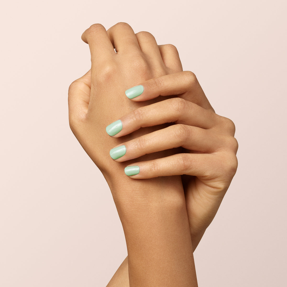 Two hands with light brown skin are gently clasped, displaying fingernails polished in Manucurist&