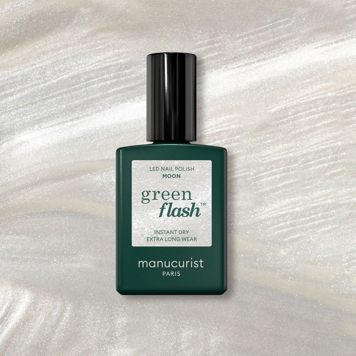 Un flacon de vernis gel Manucurist Moon repose sur un fond en marbre scintillant, son design vert foncé et son étiquette blanche mis en valeur par des touches de blanc nacré en dessous.