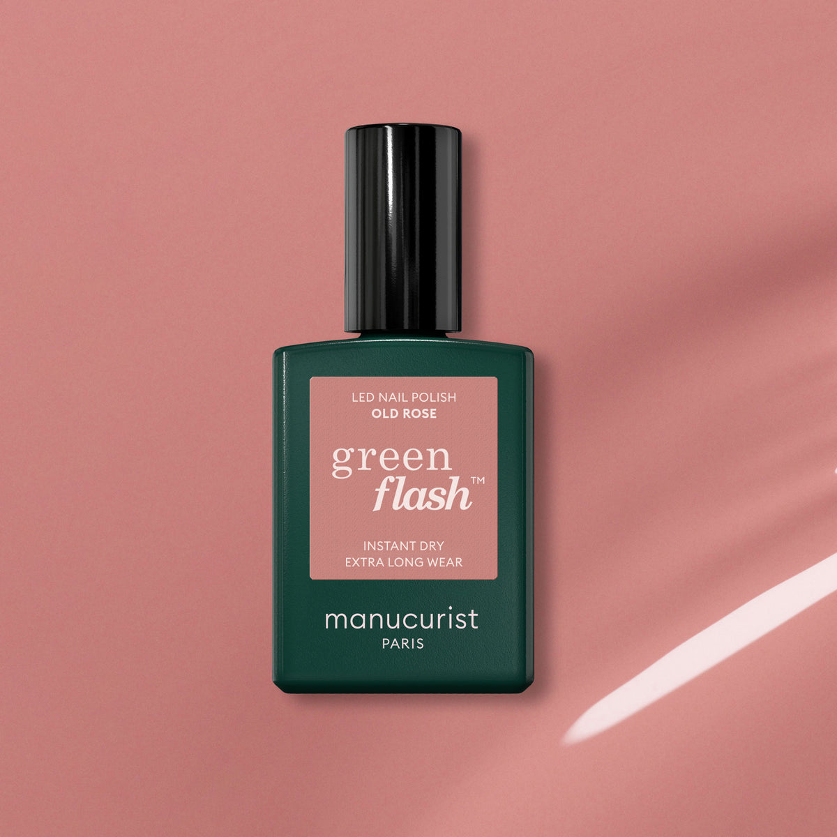 A bottle of Manucurist Old Rose, a beautiful antique pink polish, sits on a pink surface casting a soft shadow. The bottle has a dark green base and black cap.