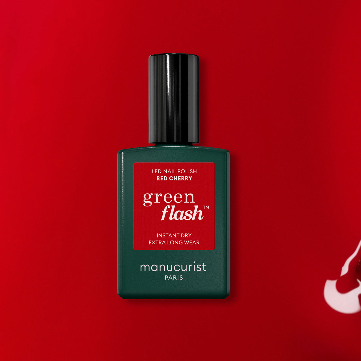 Un flacon de vernis gel Red Cherry de Manucurist est posé sur un fond rouge. Le flacon vert foncé est doté d&