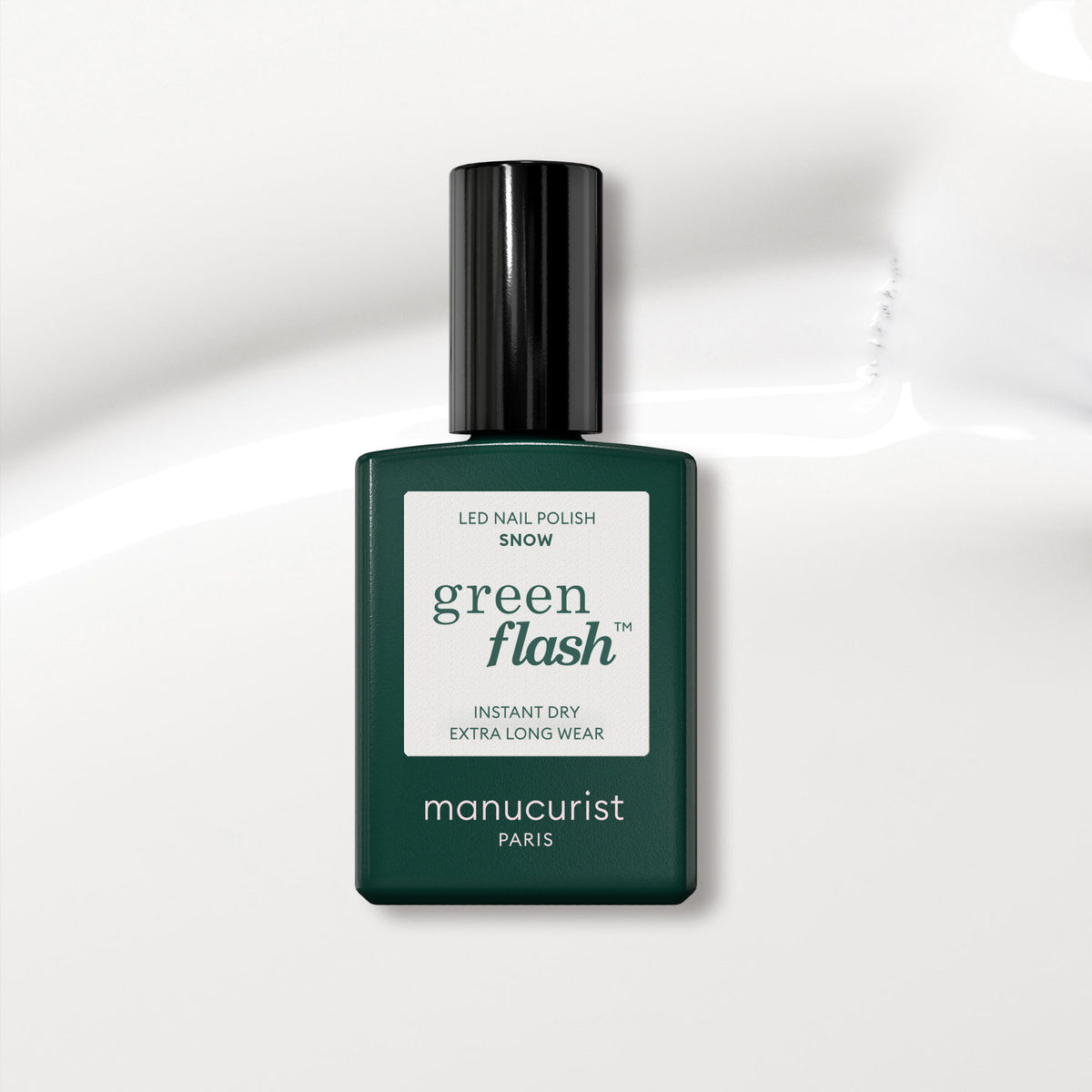 Un flacon Manucurist vert foncé de vernis gel Green Flash dans la teinte Snow est posé sur une surface blanche brillante. L’étiquette met en avant un séchage instantané et une tenue extra longue, idéale pour obtenir un look de vernis à ongles blanc pur.