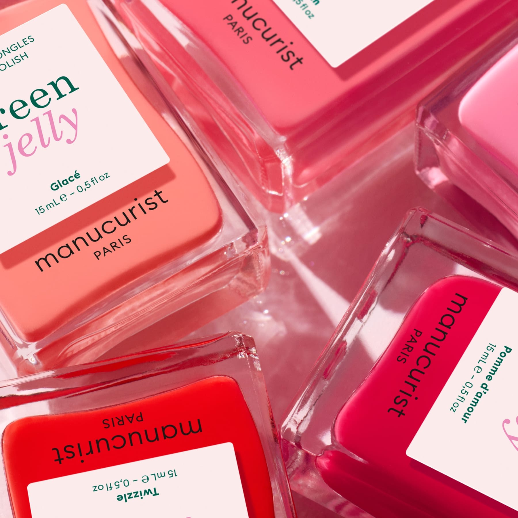 Several bottles of Manucurist Pink Sorbet Jelly nail polish in translucent pink, red, and coral shades are arranged together, displaying their rectangular glass bottles and white labels with colorful text.