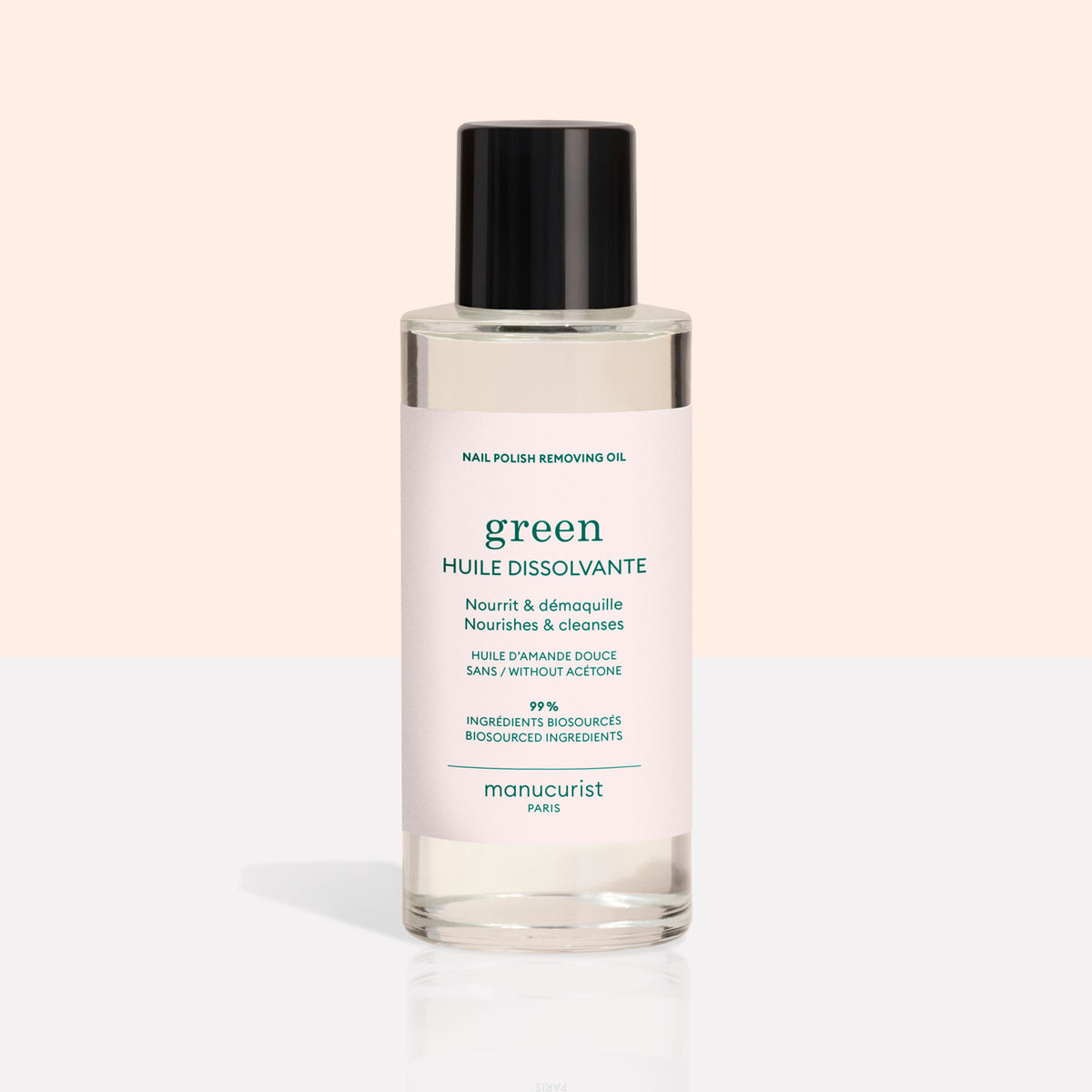 Un flacon transparent avec un bouchon noir contient l’huile dissolvante pour vernis à ongles Manucurist, une formule verte à base de plantes. Le flacon présente une étiquette rose clair avec du texte vert sur un fond beige et blanc.