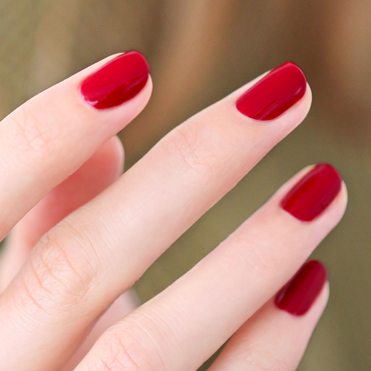 A close-up showcases neatly manicured nails coated in glossy dark red, featuring Manucurist’s Red, White  Blue Trio. The blurred background subtly highlights the trio&
