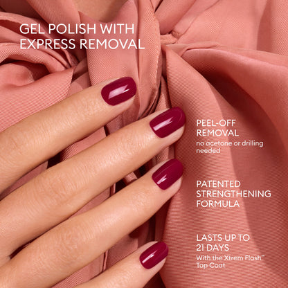 A hand with a glossy burgundy gel polish manicure, achieved with Manucurist’s Advent Calendar Time to Flash!, rests on blush pink fabric. Text highlights express removal, strengthening formula, and up to 21 days of wear. Nails appear shiny and impeccably manicured.
