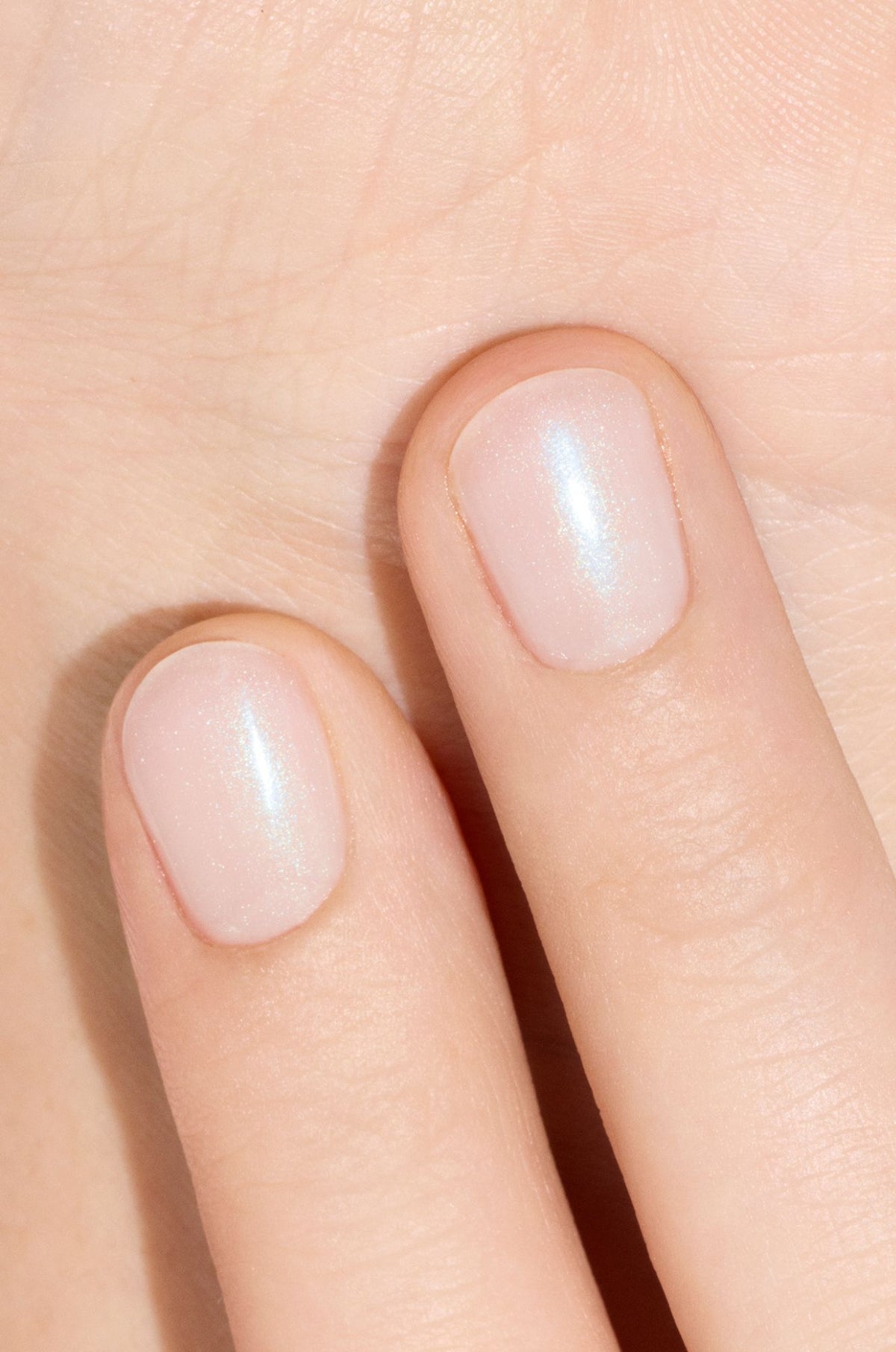 Two fingers with short, neatly filed nails painted with a pale, shimmery, pearlescent nail polish against a light skin background.