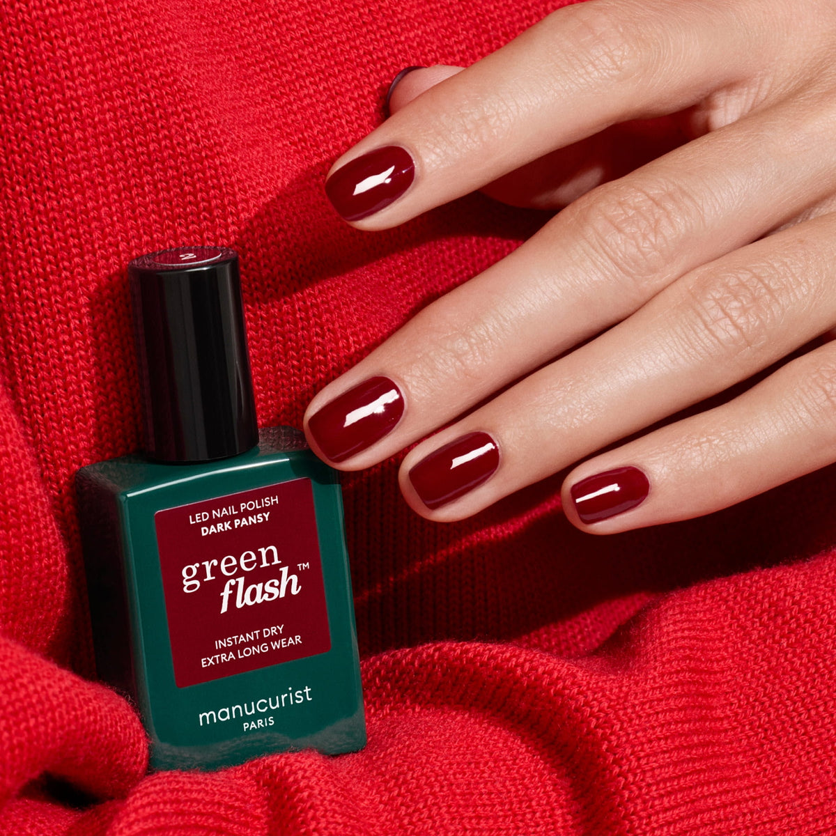 Une main aux ongles rouge foncé parfaitement manucurés repose sur un tricot rouge à côté d&