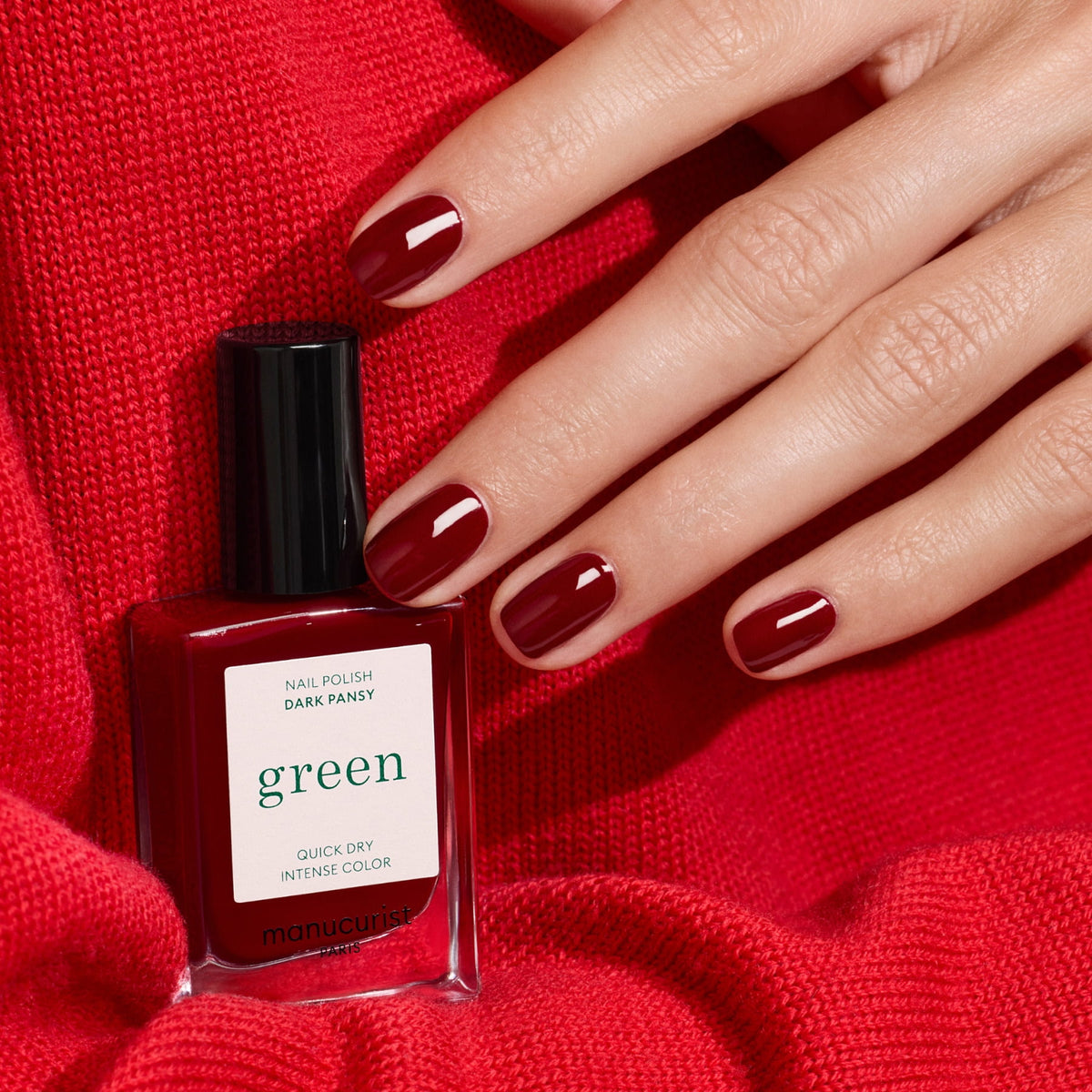 Une main aux ongles courts et soigneusement manucurés vernis de rouge velours repose sur un tissu rouge à côté d&