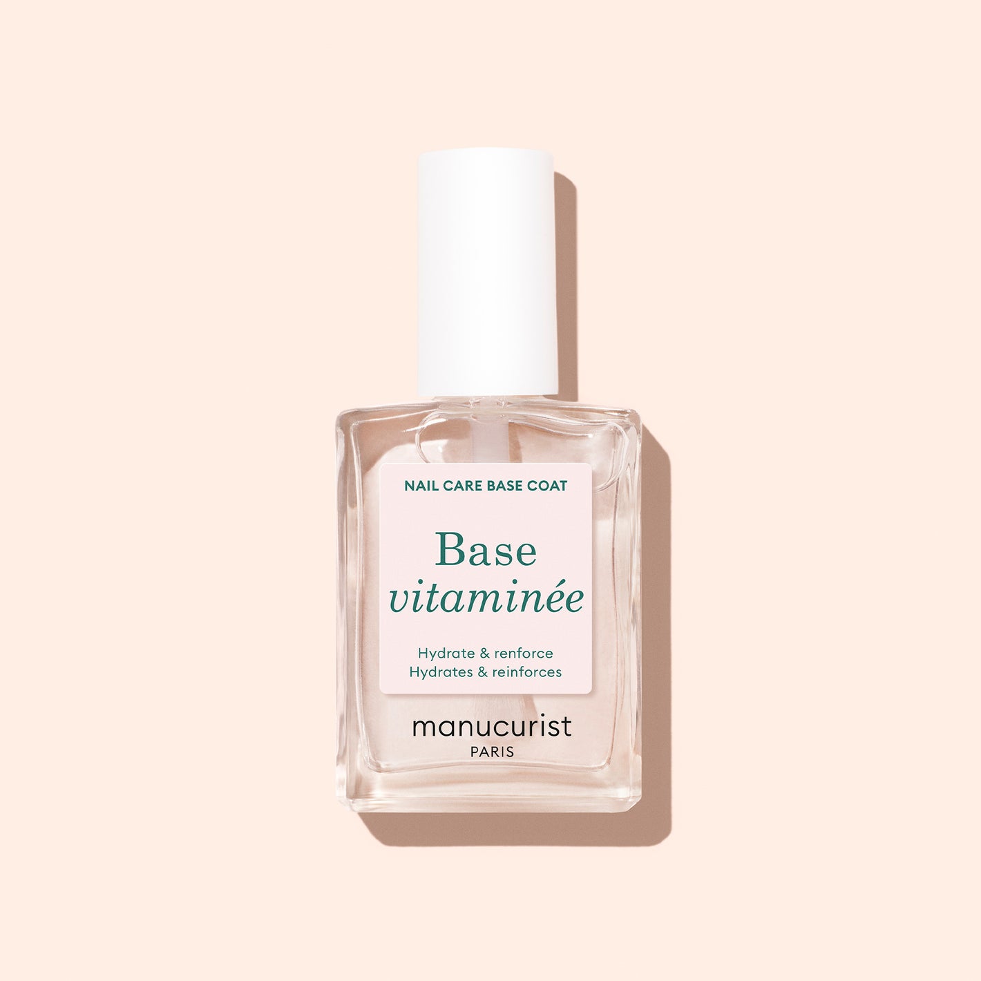 A clear glass bottle of Manucurist Vitaminized Base with a white cap rests on a light beige backdrop. This nail care base is perfect for stronger, healthier nails.
