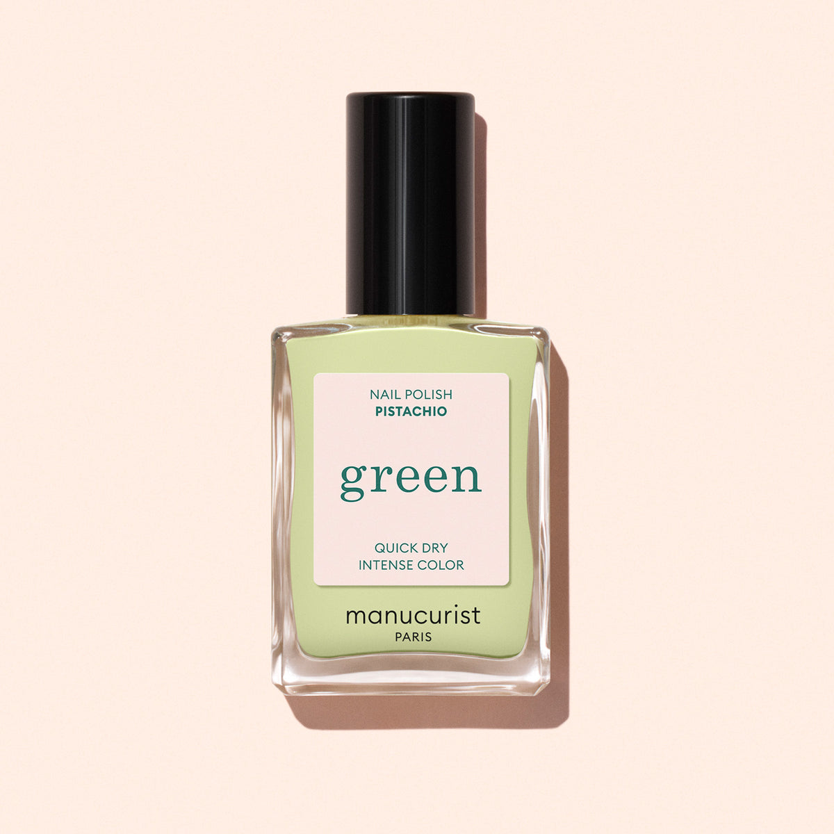 A bottle of Manucurist Pistachio nail polish from the Green™ range, featuring yellow undertones, a black cap, and labels reading “green,” “quick dry,” and “intense color,” set against a pale pink background.