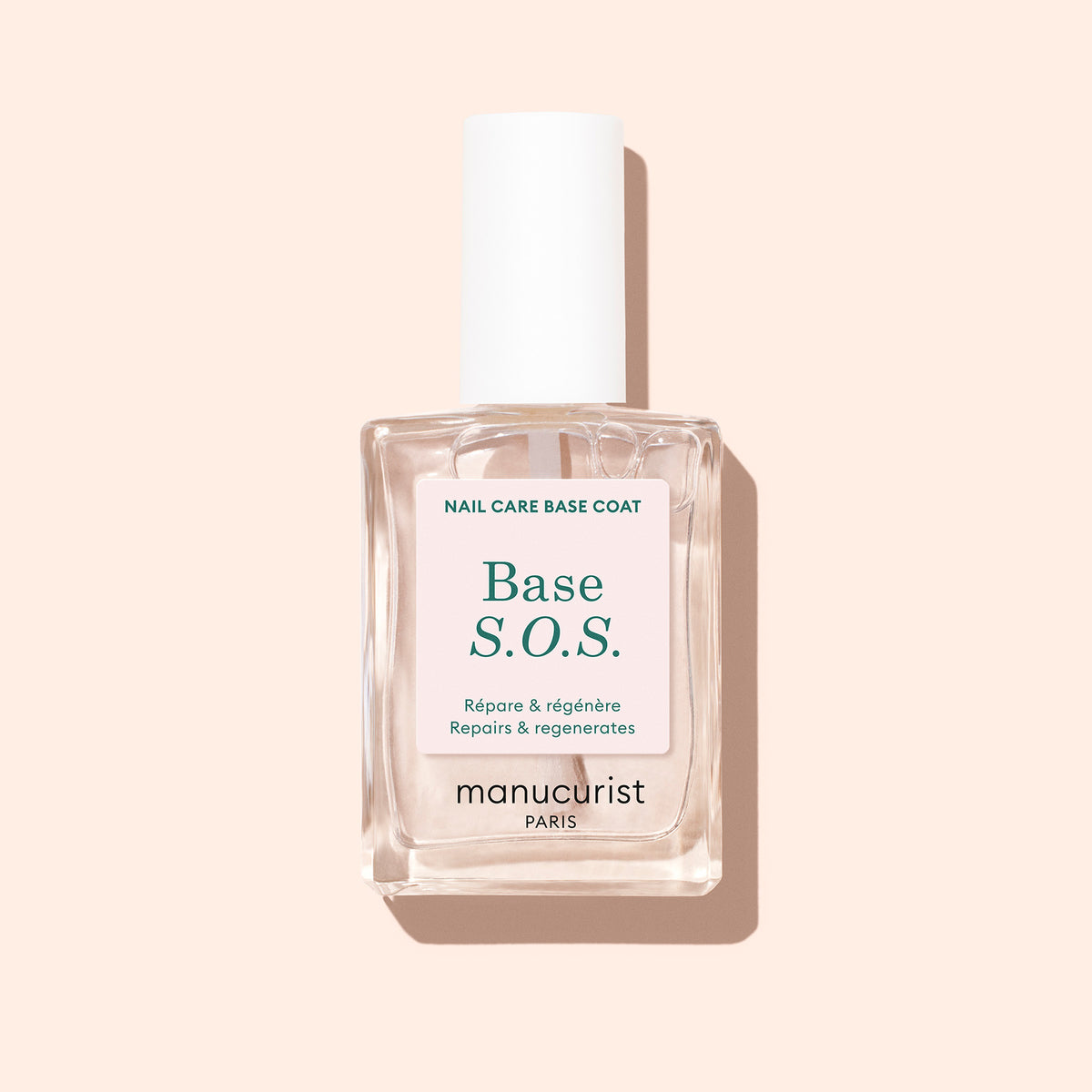 Un flacon transparent de Durcisseur S.O.S. Manucurist avec un bouchon blanc repose sur un fond beige clair, arborant une étiquette en français et en anglais indiquant "Répare régénère" — parfait pour les ongles cassants nécessitant d&