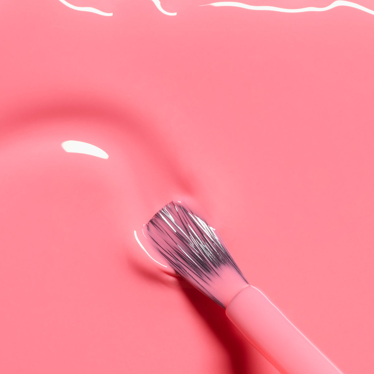 Gros plan sur un pinceau à poils souples posé sur une surface lisse recouverte du vernis à ongles Pop de Manucurist. Les reflets de lumière mettent en valeur la teinte rose électrique et la brillance glossy.