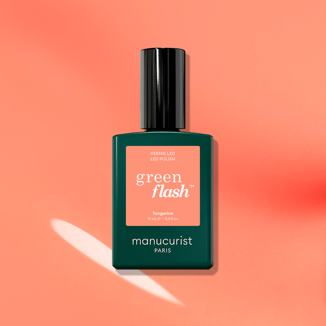 A bottle of Manucurist Tangerine gel polish, inspired by ‘90s style, is shown on a peach background with its shadow and a white light reflection.