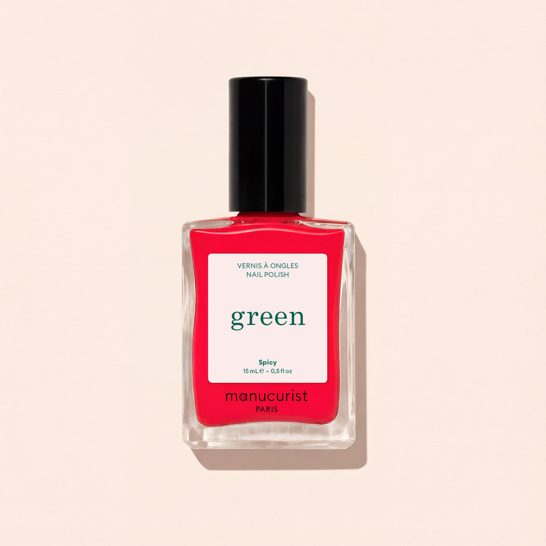 A bottle of Manucurist Spicy nail polish, a pop red shade with pink undertones from the Green™ range, features a black cap and a white label, set against a light beige background.