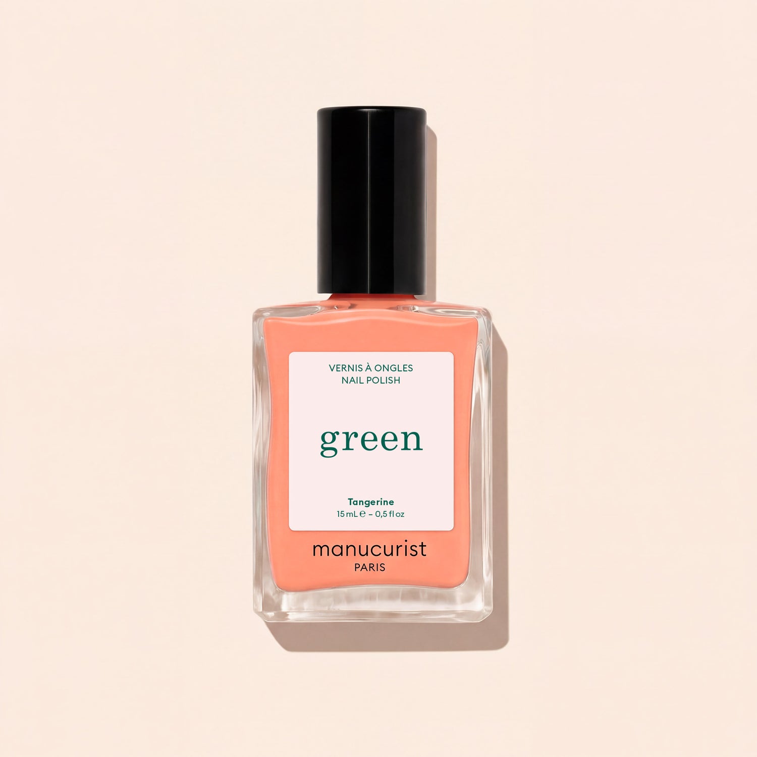 Manucurist Tangerine nail polish features a light orange shade with a black cap and white label with green and black text, shown against a light beige background. This vibrant color adds a lively pop to your look.
