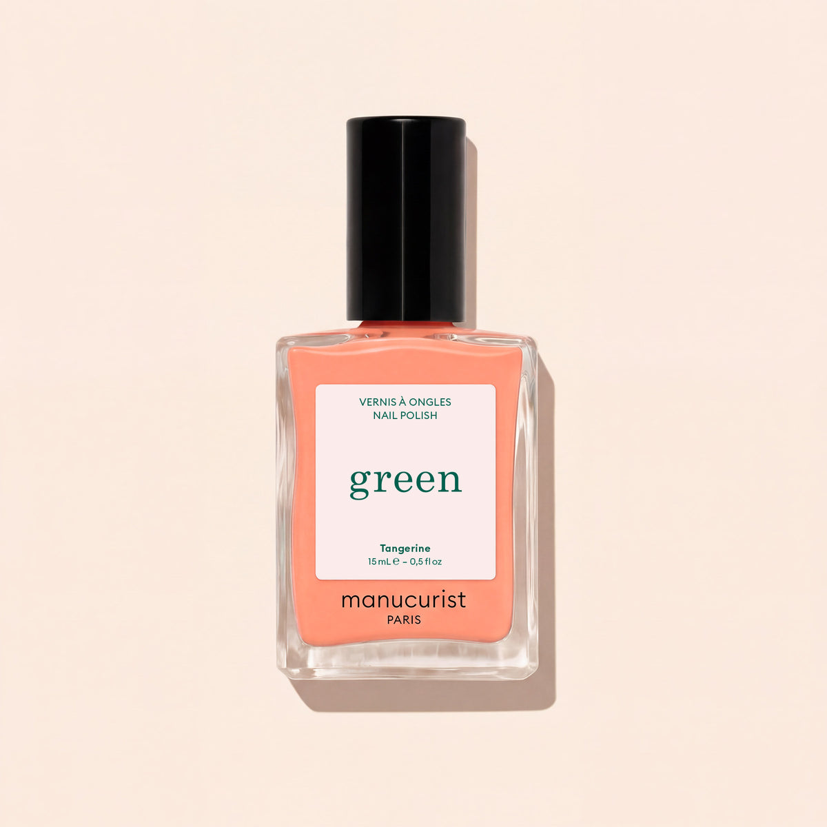 Manucurist Tangerine nail polish features a light orange shade with a black cap and white label with green and black text, shown against a light beige background. This vibrant color adds a lively pop to your look.