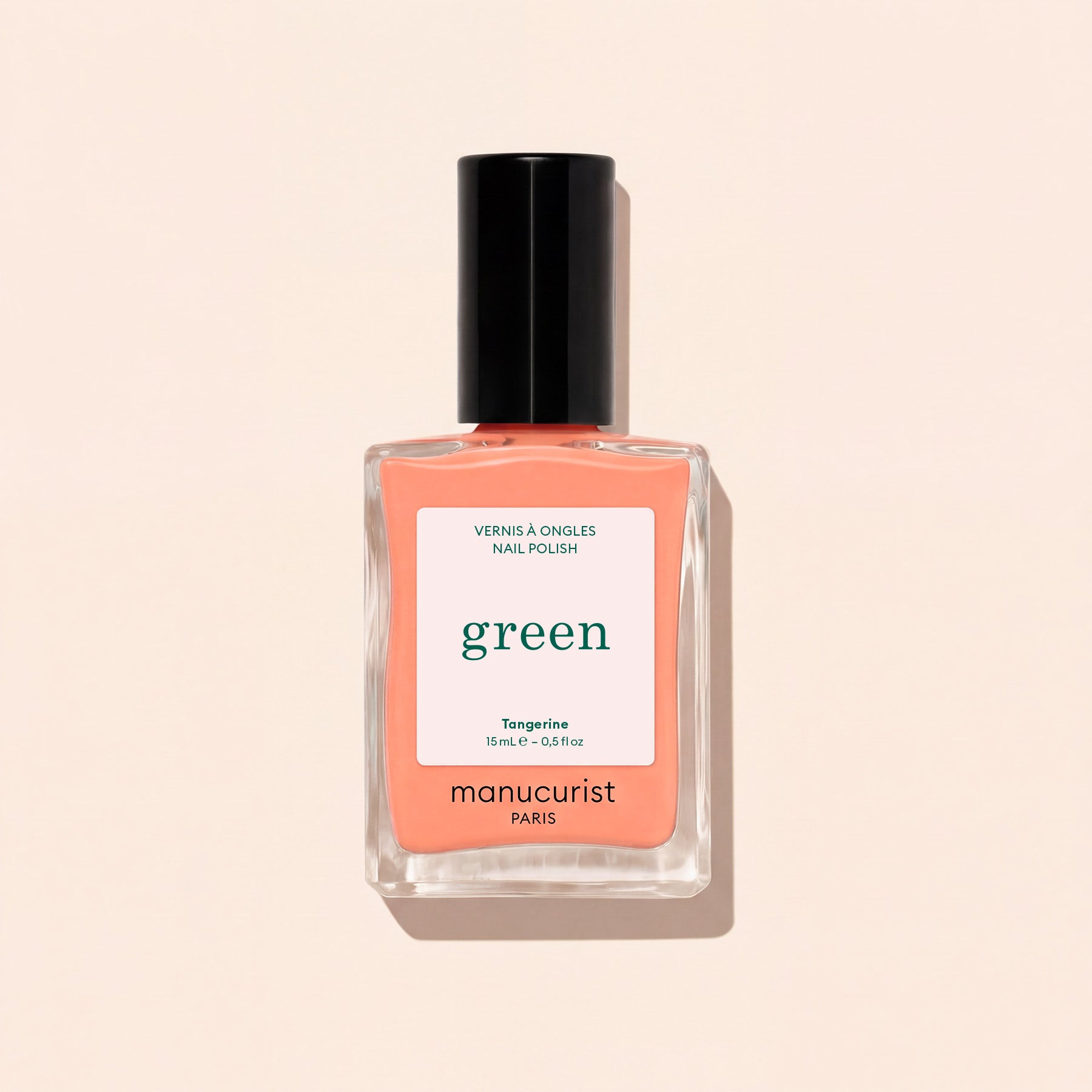 Manucurist Tangerine nail polish features a light orange shade with a black cap and white label with green and black text, shown against a light beige background. This vibrant color adds a lively pop to your look.