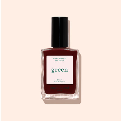 A bottle of Manucurist Grenat nail polish from the Green range, with a black cap, is displayed against a light beige background. The label reads “green” and “Nail Polish,” highlighting this earthy maroon red shade.