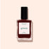 A bottle of Manucurist Grenat nail polish from the Green range, with a black cap, is displayed against a light beige background. The label reads “green” and “Nail Polish,” highlighting this earthy maroon red shade.