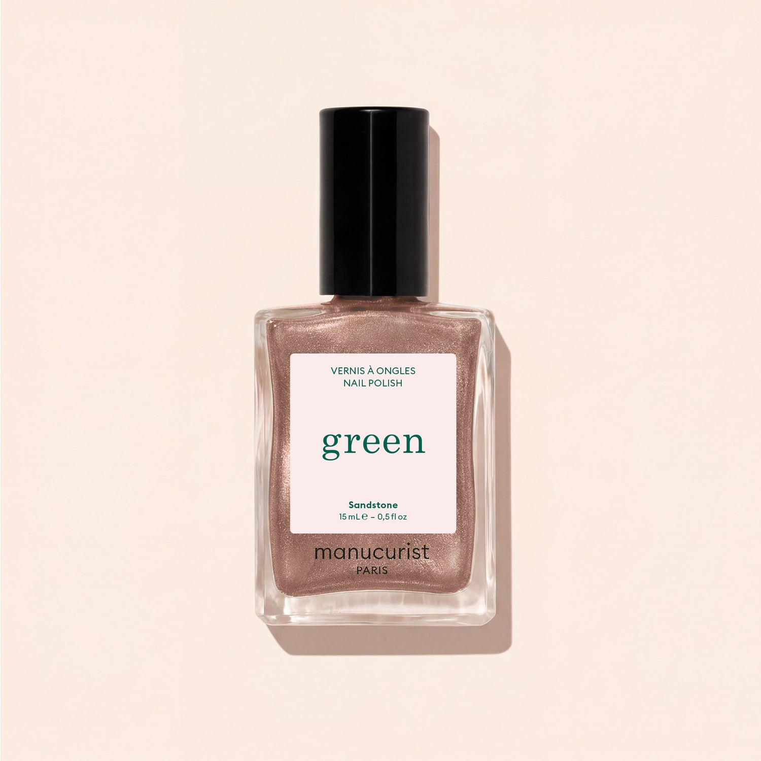 A bottle of Manucurist nail polish in the shade Sandstone, a shimmery rose gold hue, displayed against a light beige background.