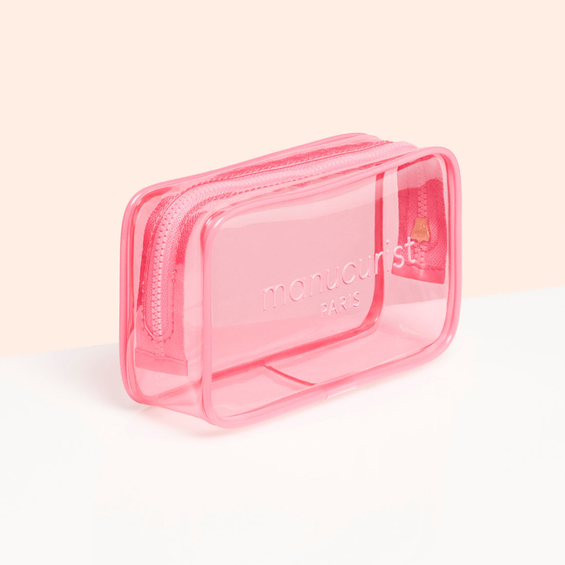The Mini Jelly Bag by Manucurist is a small, rectangular, transparent pink bag with "manucurist PARIS" on the front—ideal for travel manicure kits or nail polish storage. Shown on a white surface with a pale peach backdrop.