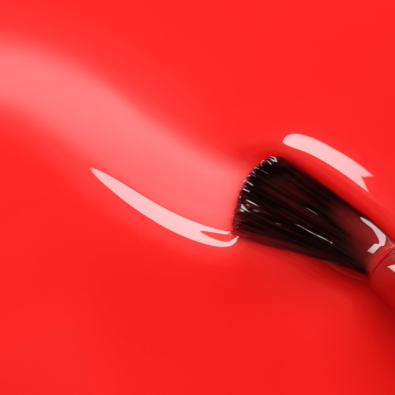 A Manucurist Twizzle brush glides through translucent red polish, creating a smooth, vibrant streak on the ultra-glossy surface.