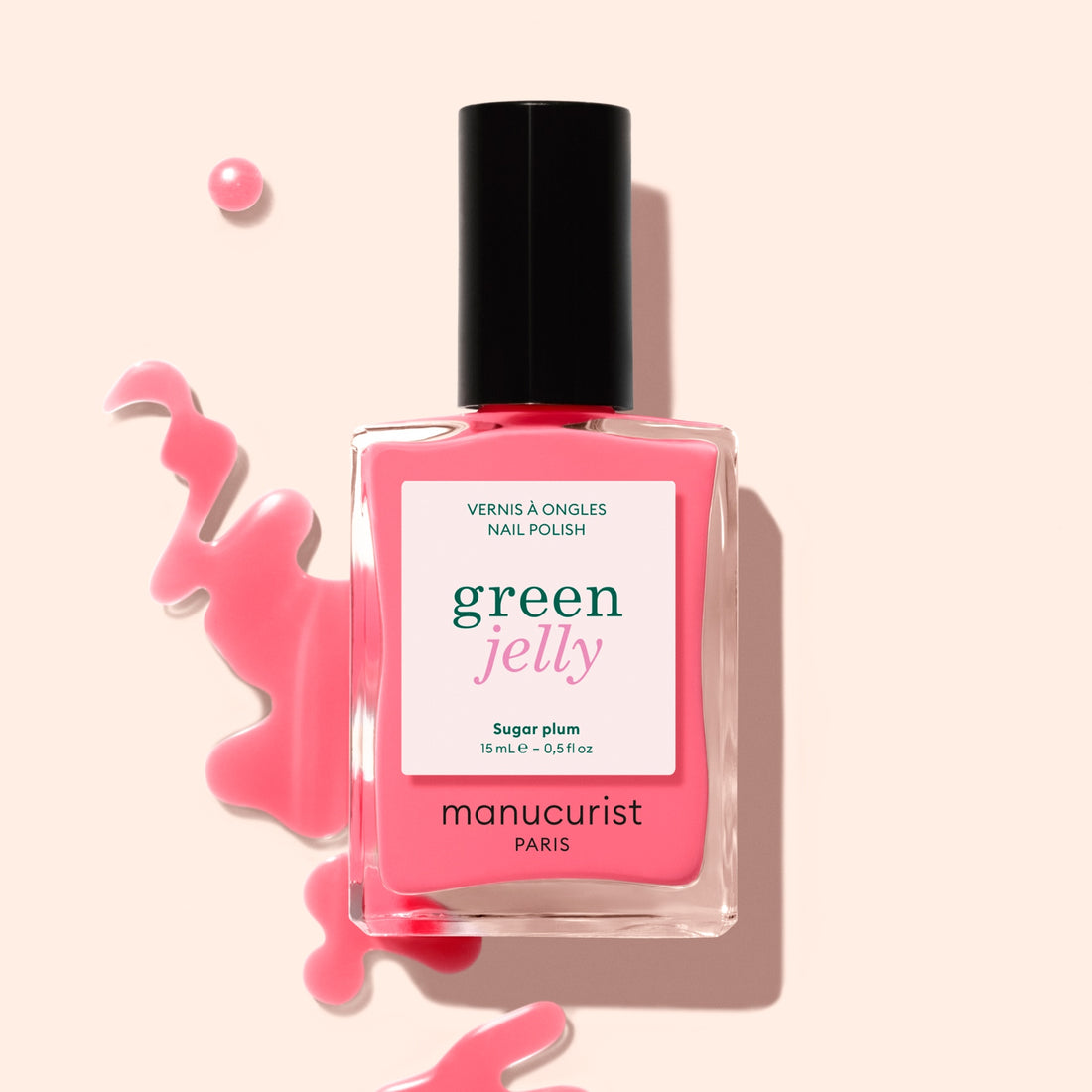 A bottle of Manucurist Sugar Plum Jelly nail polish, a translucent pink shade, sits beside an ultra-glossy spill on a light beige background.