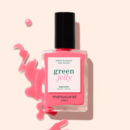 A bottle of Manucurist Sugar Plum Jelly nail polish, a translucent pink shade, sits beside an ultra-glossy spill on a light beige background.