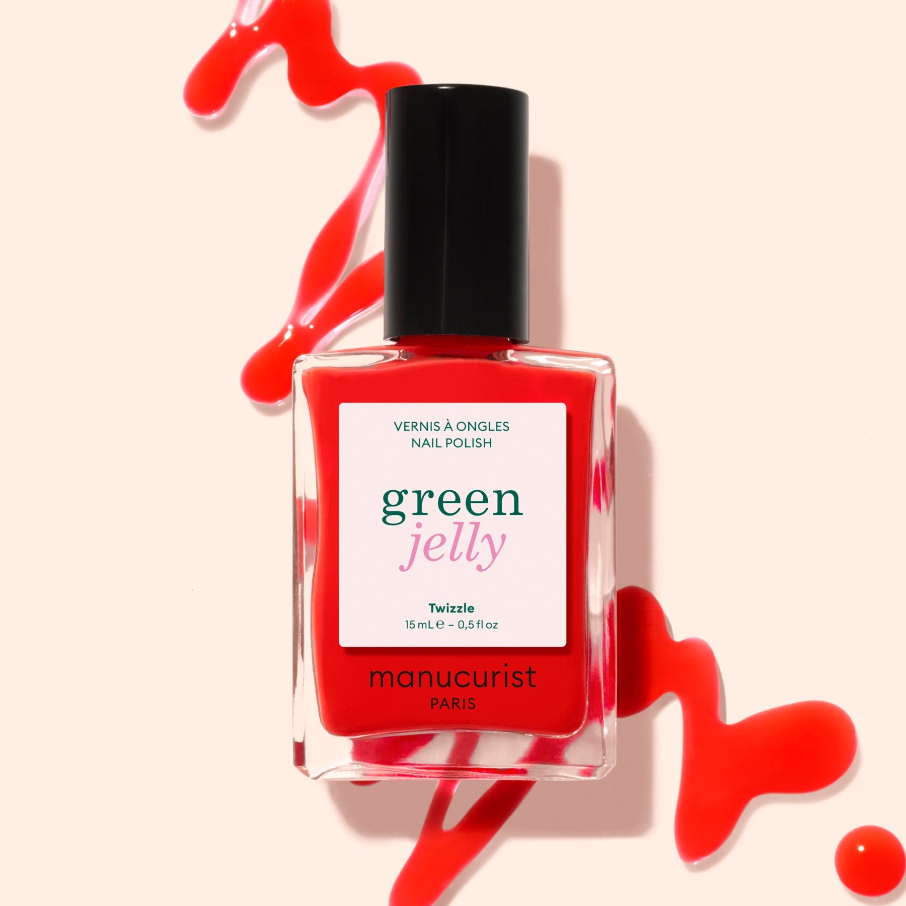 A bottle of Manucurist Twizzle Jelly nail polish in translucent red is displayed, with the red polish spilled artistically around it on a light background.