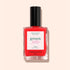 A bottle of vivid red, ultra-glossy Manucurist Twizzle jelly nail polish with a black cap and a white label featuring red and green text rests on a light beige background.