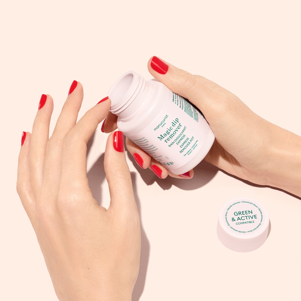 A person with red nail polish holds an open white bottle labeled Magnesium capsules by Green  Active against a light pink background, with the bottle cap nearby.