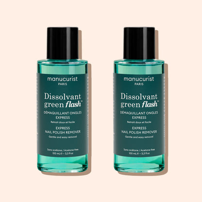 Two identical bottles of Manucurist Green Flash™ Gel Polish Remover with teal liquid, black caps, and white labels stand side by side on a beige background.