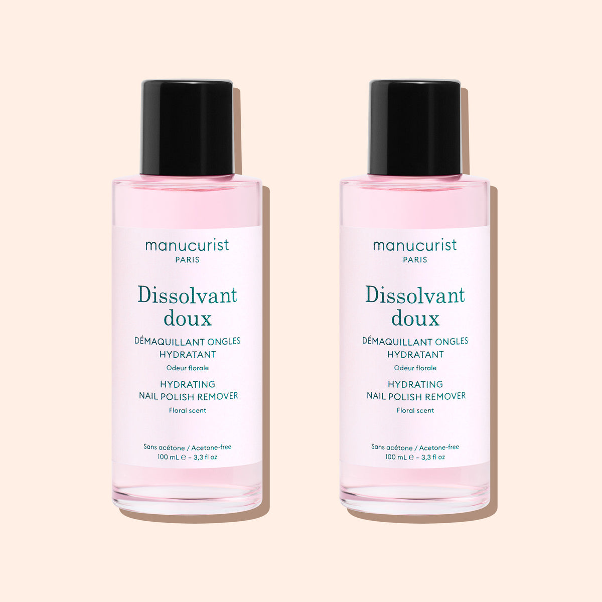 Deux flacons de Gentle Remover Manucurist, avec un liquide rose pâle sans acétone, des bouchons noirs et des étiquettes blanches, sont placés côte à côte sur un fond beige clair.